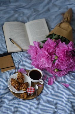 Kahve, kruvasan ve peonies yatakta okuma