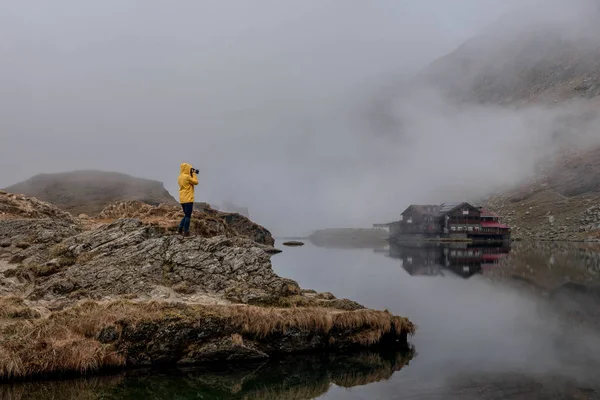 シャトーと湖の写真を撮る黄色のジャケットの女性旅行者 ストック写真