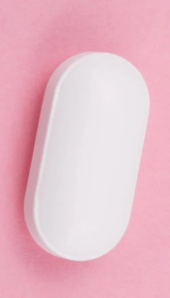 Белая таблетка на розовом фоне — стоковое фото
