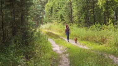 Bir kız ve bir köpek yavrusu bir orman yolu yürüyor