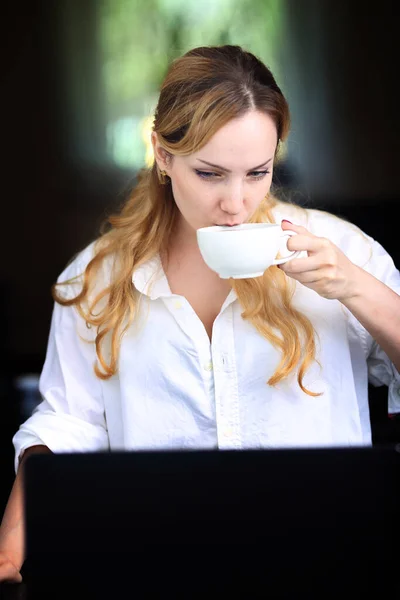 一个沉默寡言 面带微笑的女人 一杯咖啡和一台电脑 — 图库照片