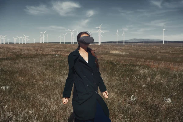 Mulher vestindo fone de ouvido VR no campo ao lado das turbinas eólicas — Fotografia de Stock