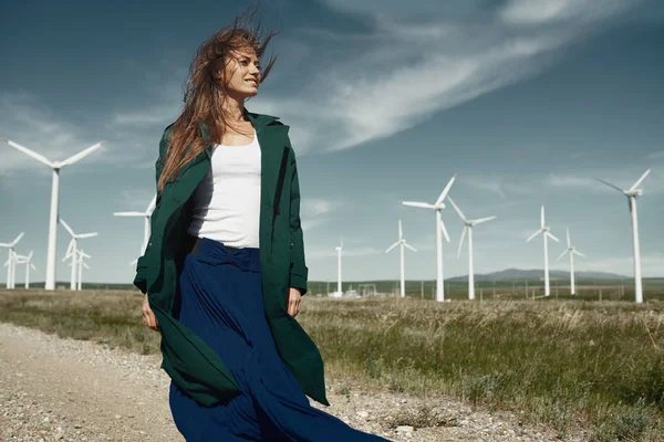 Kvinna med långt rufsigt hår bredvid vindkraftverk med w — Stockfoto