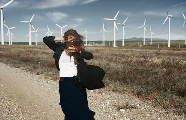 Woman with long tousled hair next to the wind turbine with the w