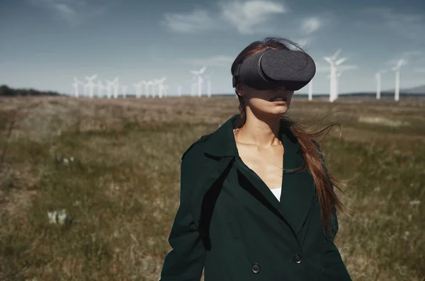 Rüzgar türbinlerinin yanındaki tarlada VR kulaklık takan kadın. Stok Resim