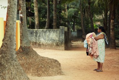 Olgun bir Hintli kadının elinde çarşaf ve ormanlarda evinin yanında dikilirken çekilmiş resmi. Goa, Hindistan