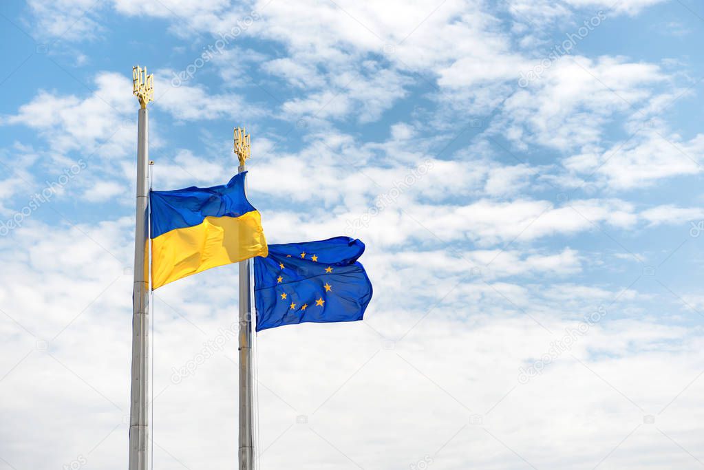 Flags of Europe and Ukraine on the poles with blue sky as background