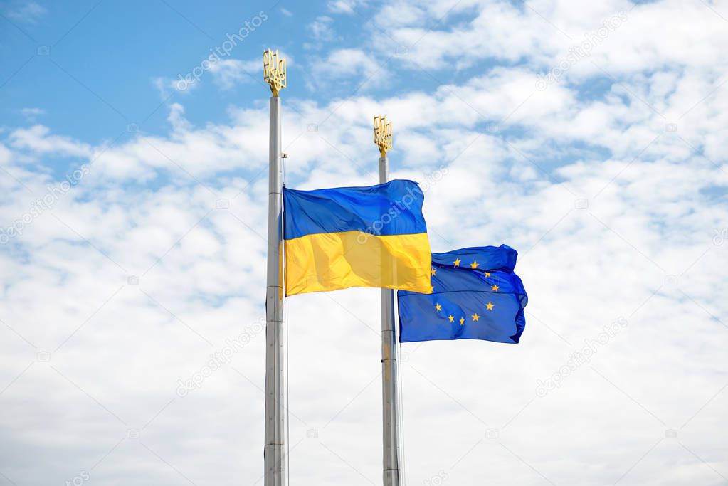 Flags of Europe and Ukraine on the poles with blue sky as background