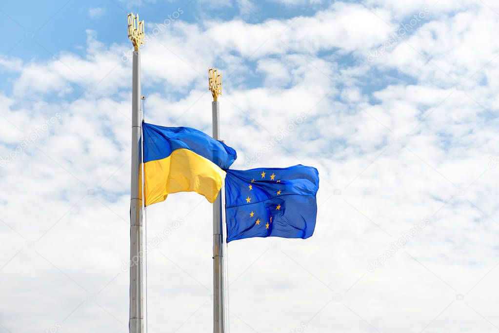 Flags of Europe and Ukraine on the poles with blue sky as background