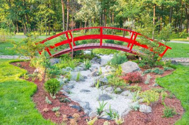 Yeşil parktaki güzel çiçek tarhının üzerindeki kırmızı Japon köprüsü.