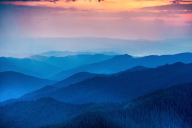 Tepeler ve dramatik renkli gökyüzü ile dağlarda günbatımı