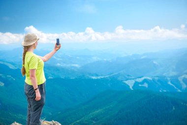 Dağlar cliff üzerinde duran ve seyahat selfie smartphone alarak genç kadın
