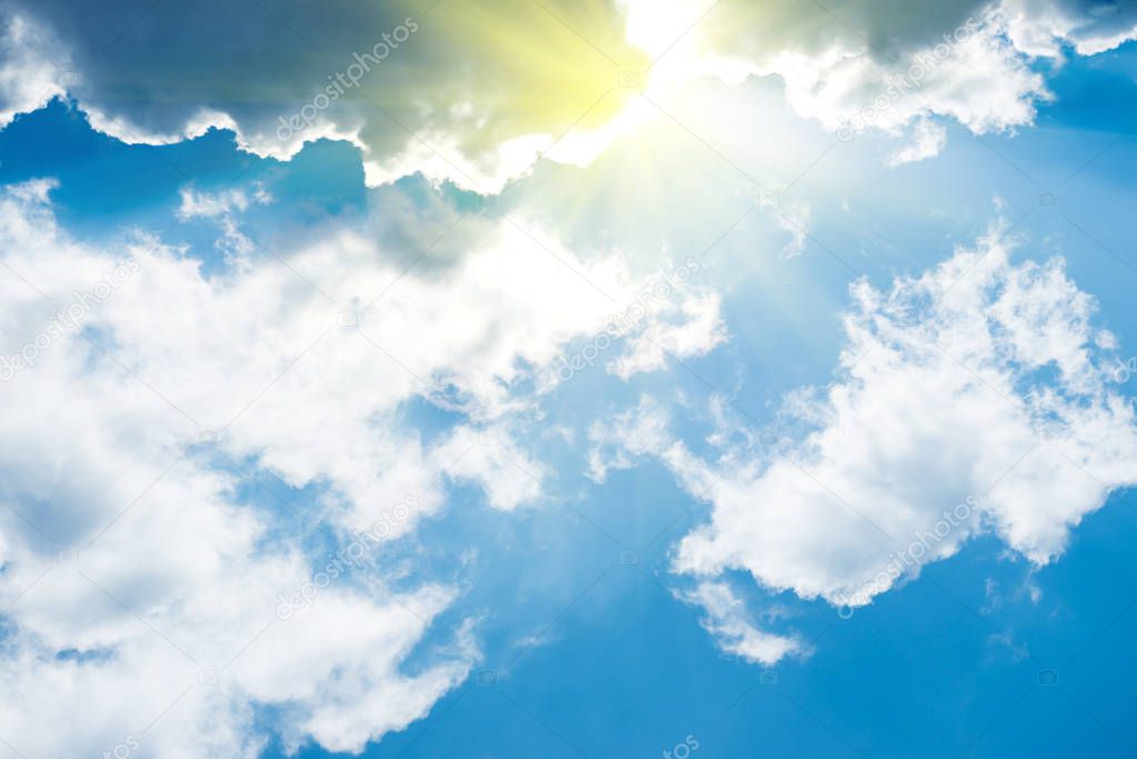 White fluffy clouds on the blue sky with sun rays. Nature background