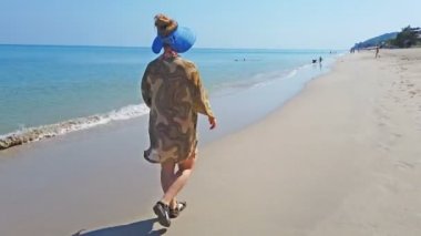 Sarı kum ve deniz su ile bir sahilde yürüyen kadın. 