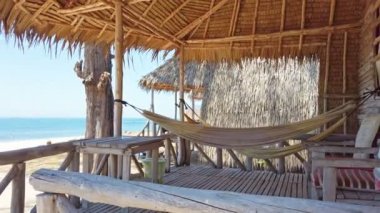 Tropik adada kayalar ile kum plaj manzarası ve hamaklar ve ahşap mobilya ile bungalov.