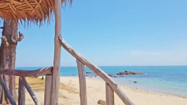 Tropik adada kayalar ile kum plaj manzarası ve hamaklar ve ahşap mobilya ile bungalov.