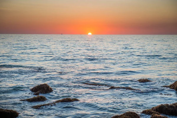 Sonnenuntergangslandschaft mit goldener Sonne und Steinen am Meer — Stockfoto