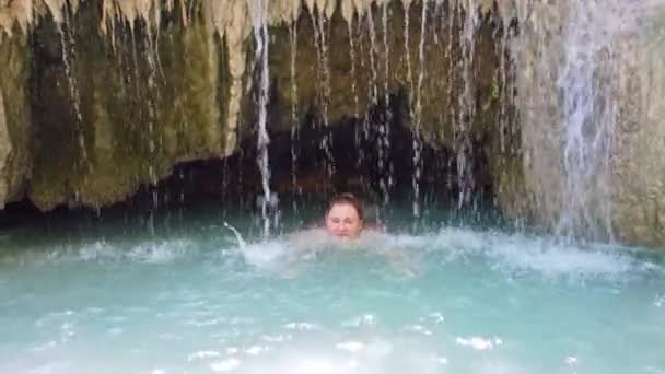一个红头发的年轻漂亮的女人在瀑布下的蓝水湖中游泳 4K视频剪辑 — 图库视频影像