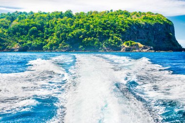 Mavi deniz ve yeşil ada kıyıları olan su yüzeyinde ve ufukta deniz teknesinin uyanışı.