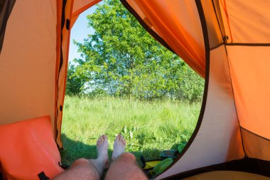 Turuncu çadırda yeşil çimenli yeşil çimlere uzanan bir adam.