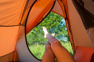 Turuncu çadırda yeşil çimenli yeşil çimlere uzanan bir adam.