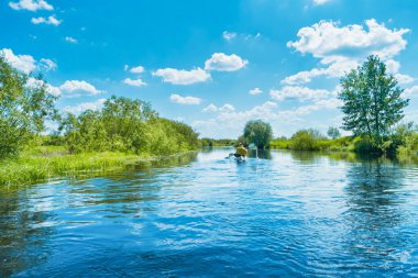 Mavi nehir manzarasında kano gezisindeki çift ve ağaçlı yeşil orman mavi su bulutları gökyüzünde