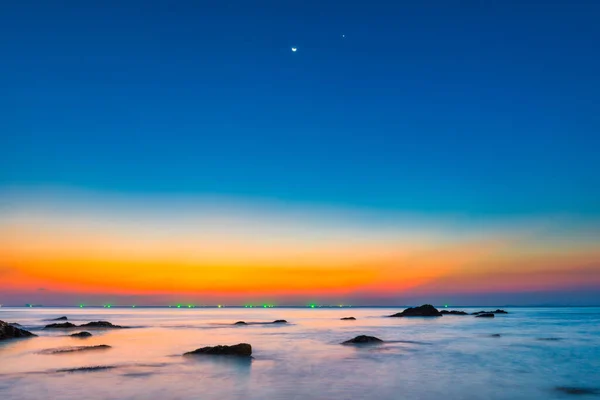 月の光の下で劇的な空に岩や夕日の夜の風景と日没の海 — ストック写真