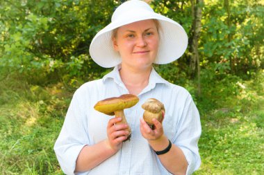 Ormanda elinde büyük Boletus Edulis ya da Penny Bun mantarları olan güzel bir genç kadın.