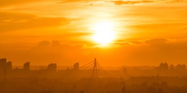 Şehir manzarası, büyük şehirde gün batımı, modern köprü ve dramatik günbatımı gökyüzü altındaki binalar.