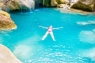 Pembe bikinili kızıl saçlı genç kadın tropik gölün zümrüt mavisi sularında yüzüyor. Erawan Ulusal Parkı, Kanchanaburi, Tayland