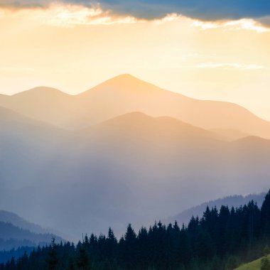 Dağlarda güzel bir gün batımı. Turuncu bulutların arasından parlayan güneşli manzara