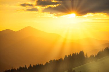 Dağlarda güzel dramatik bir gün batımı. Gün batımı dağlarının manzarası, bulutların arasından güneş ışığı...