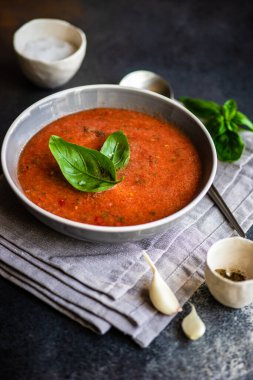 Traditional spanish tomato soup Gazpacho derved in ceranic bowl with fresh basil leaves on stone background with copy space clipart