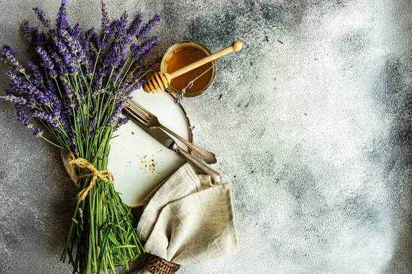 Summer time table set with minimalistic stoneware and cutlery served on concrete background and decorated with fresh lavender flowers