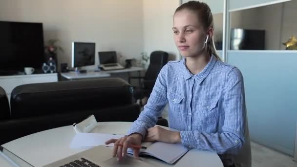 Junge Studentin hört während der Prüfungsvorbereitung Musik und macht sich Notizen im Notizbuch — Stockvideo