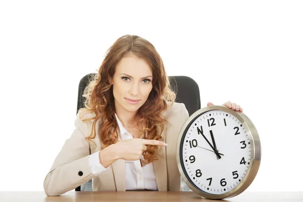 Donna d'affari che punta su un orologio da una scrivania . Immagini Stock Royalty Free