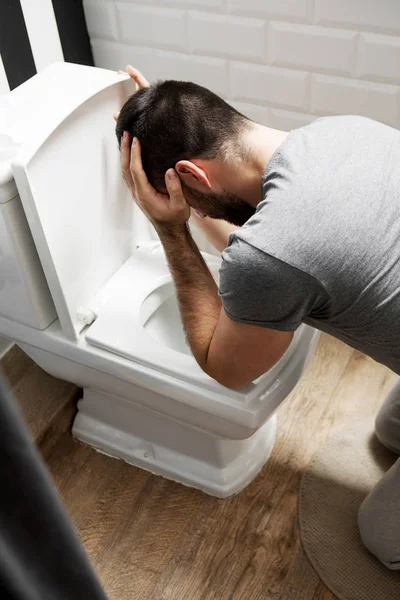 Muž sedí poblíž záchod a zvrací — Stock fotografie