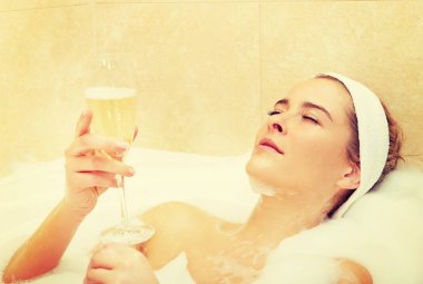 Kadın bir bardak şampanyayla banyoda dinleniyor.