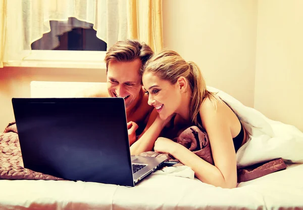 Молодая пара использует ноутбук в постели — стоковое фото