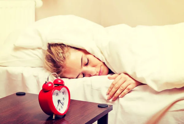 Młoda kobieta próbuje zasnąć, gdy dzwoni budzik. — Zdjęcie stockowe