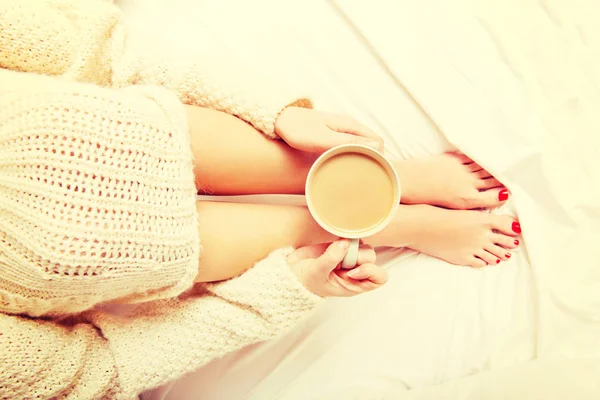 Mujer joven sentada en la cama con una taza de café — Foto de Stock