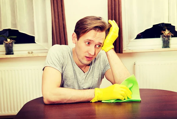 Tired man sitting behind the desk with cloth and gloves — Stock Photo, Image