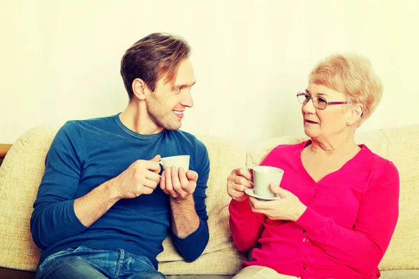 Мать и сын сидят на диване и пьют чай или кофе — стоковое фото