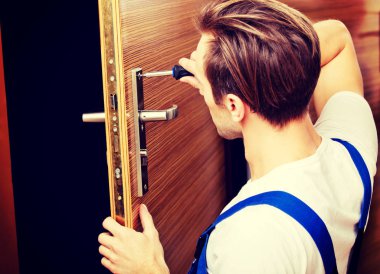 Genç adam tornavidayla kapıyı tamir ediyor.