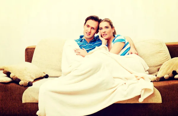 Улыбающаяся любящая пара, сидящая на диване с одеялом — стоковое фото