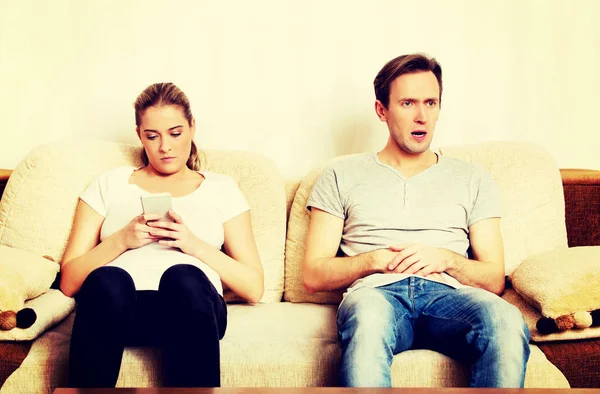 Paar zu Hause, Mann sieht Fernsehfrau mit Smartphone zu — Stockfoto