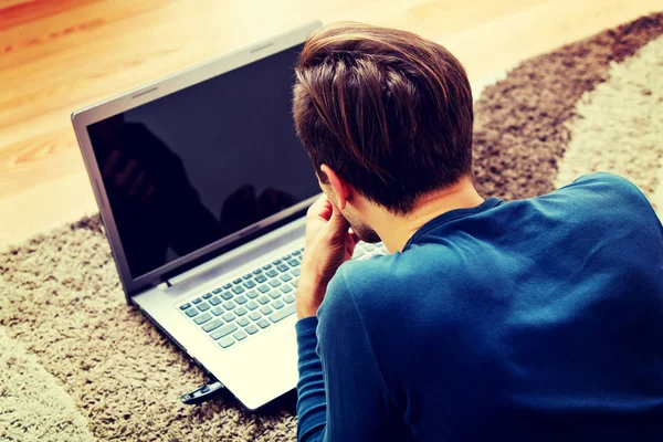 Ung man som ligger på golvet och använder laptop — Stockfoto