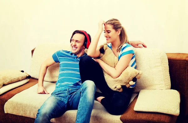 Couple relaxing on the sofa, man listening music woman hugging him — Stock Photo, Image