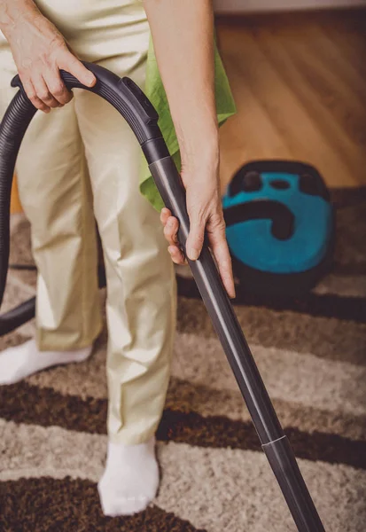 Elderly woman doing woman chores. Vacumming the carpet — Stock Photo, Image