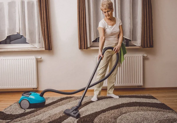 年配の女性が掃除機をかける — ストック写真